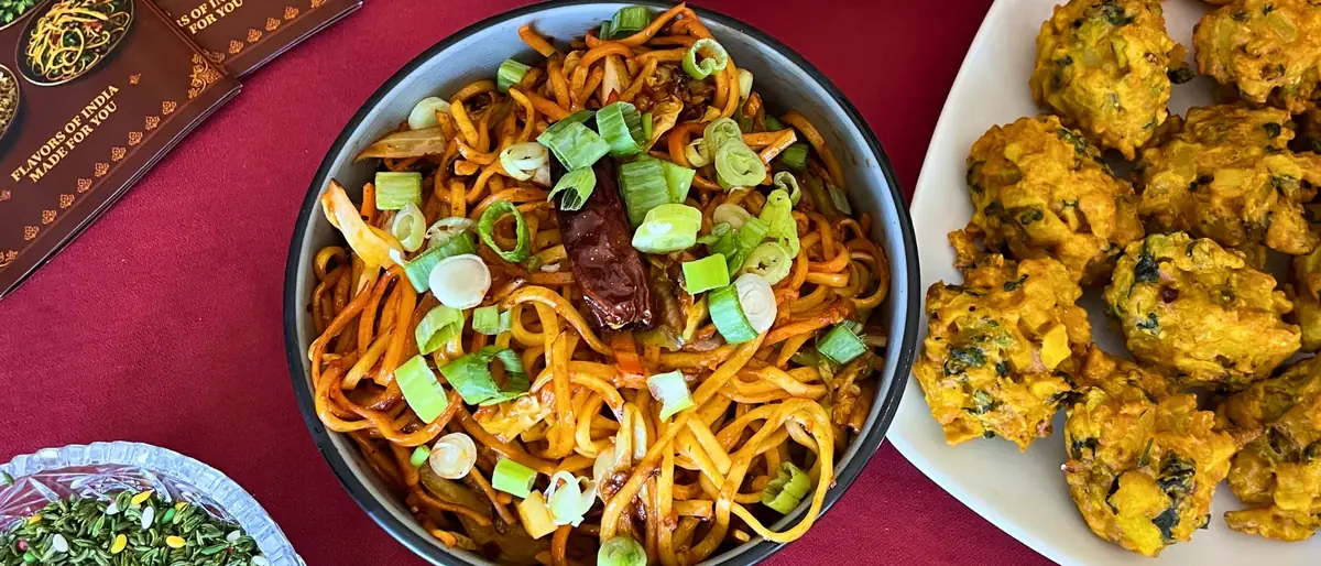 A flatlay of hakka noodles beside a plate of vegetable pakora and a Delhi Palace menu card