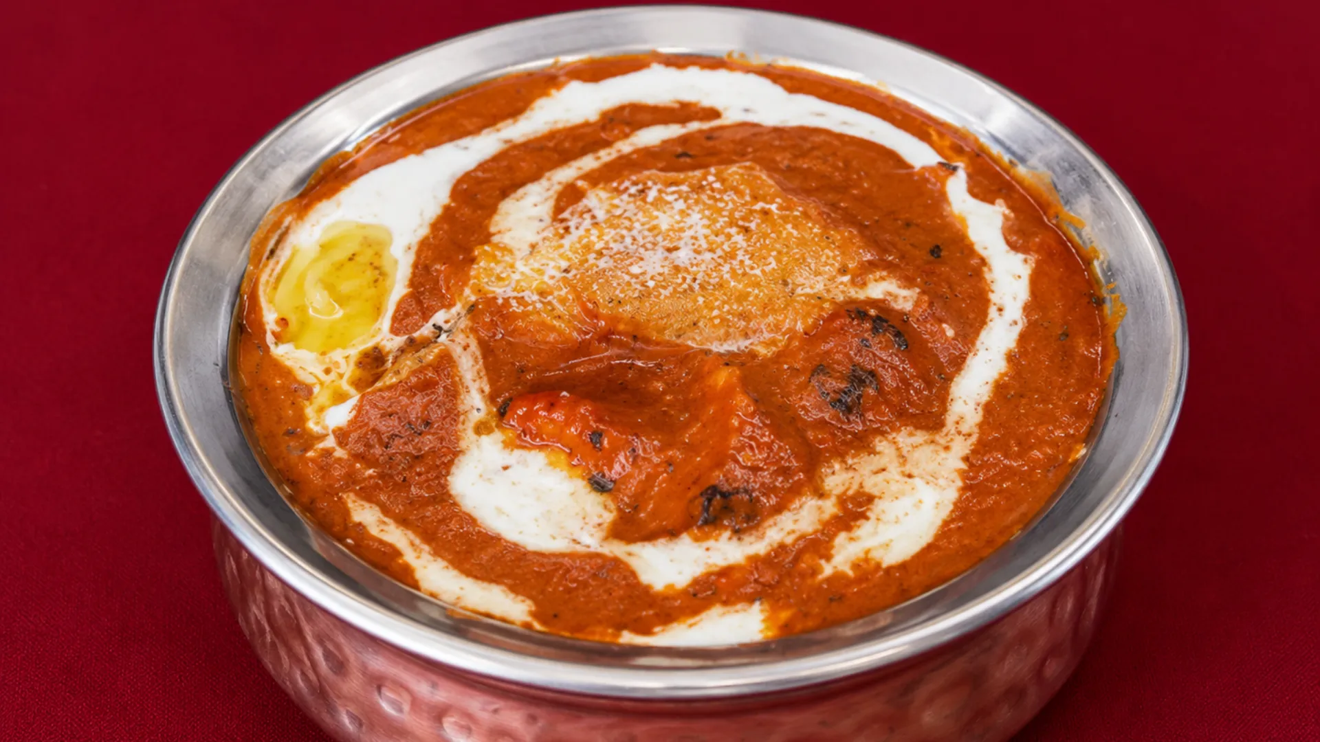 Butter chicken swirled with cream in a hammered copper bowl at Delhi Palace Brantford