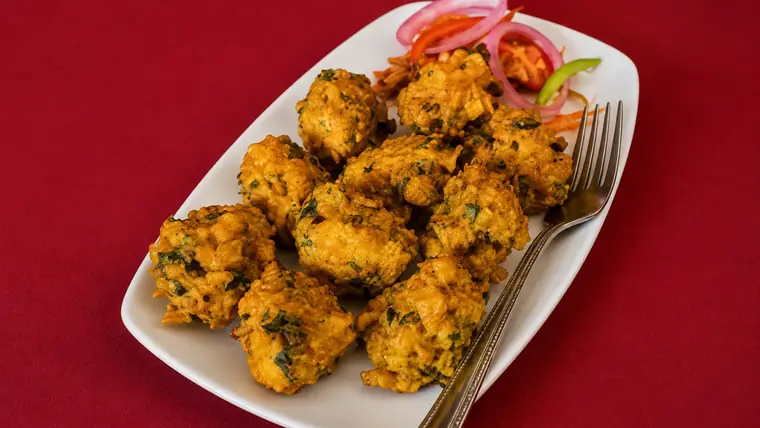 A platter of golden vegetable pakora garnished with red onion