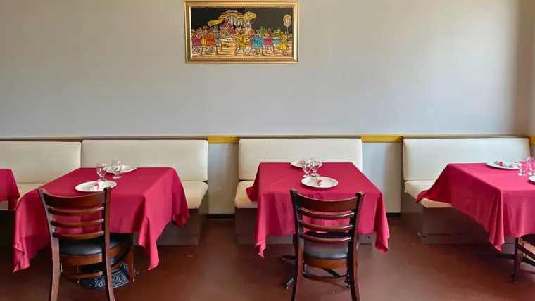 The Delhi Palace dining room with red linen tables, cream booth seating and framed Indian artwork