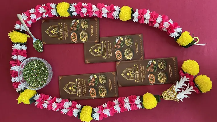 Delhi Palace menu cards arranged inside a marigold garland on a red tablecloth