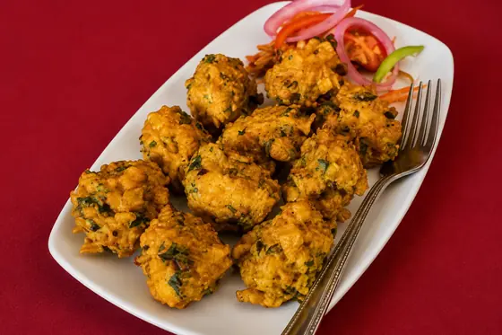 A platter of golden vegetable pakora garnished with red onion