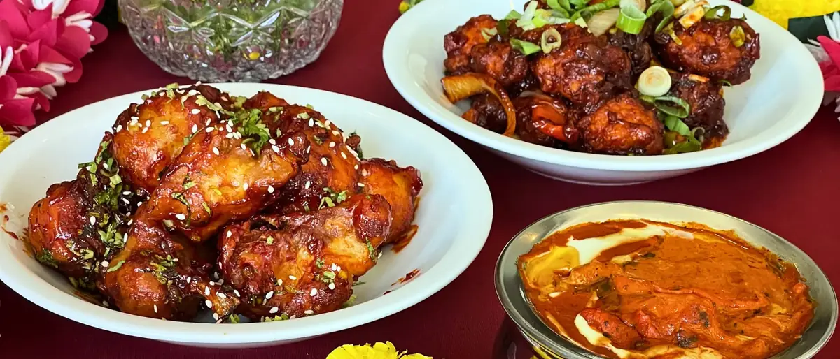 Tandoori wings, chilli chicken and a copper bowl of curry laid out on a red table at Delhi Palace